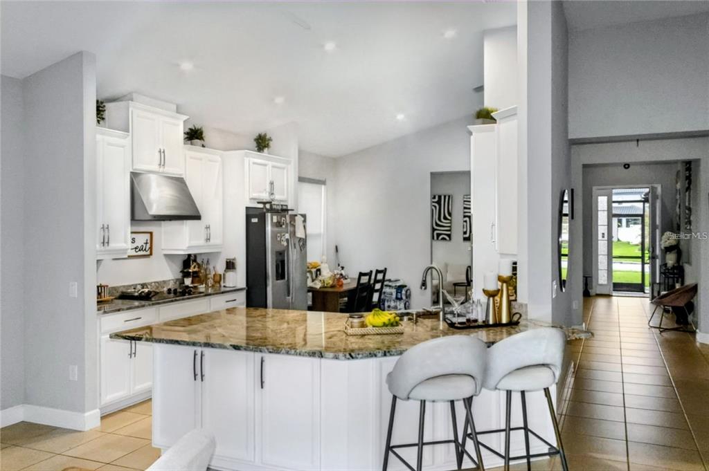 A white kitchen features a granite-topped island with two stools and stainless steel appliances — 3958 CARRICK BEND DRIVE, KISSIMMEE, FL