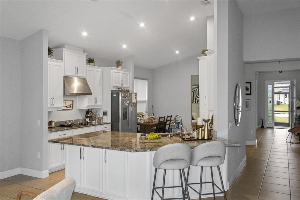 A kitchen features white cabinets, granite countertops, a central island, and two grey bar stools — 3958 CARRICK BEND DRIVE, KISSIMMEE, FL