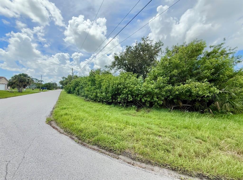 A paved road curves alongside a grassy lot bordered by dense green trees and shrubs — 6057 BOWIE LANE, ENGLEWOOD, FL