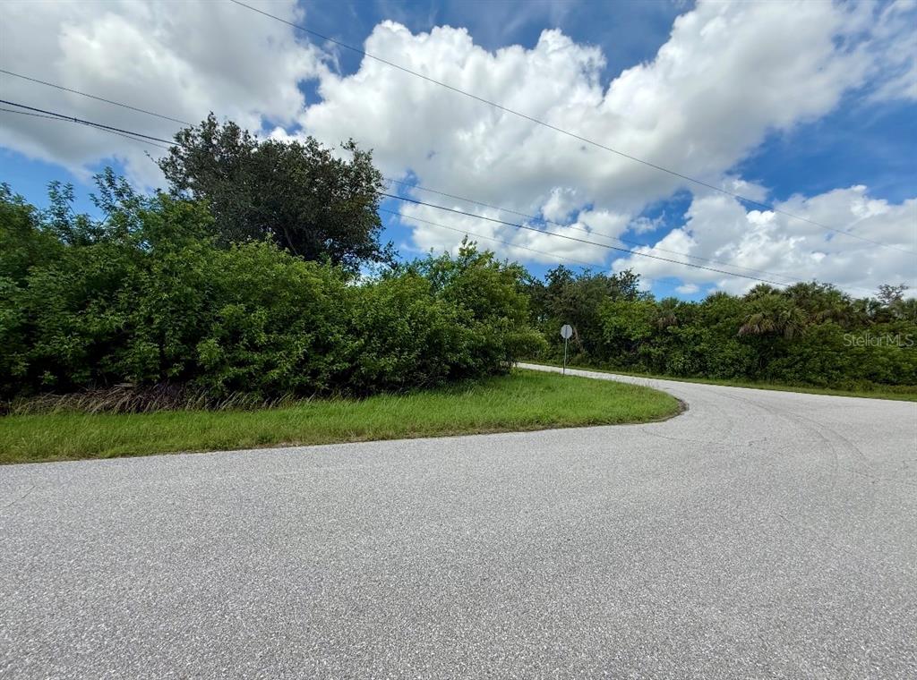 A paved road curves past a grassy area bordered by dense trees and shrubs — 6057 BOWIE LANE, ENGLEWOOD, FL