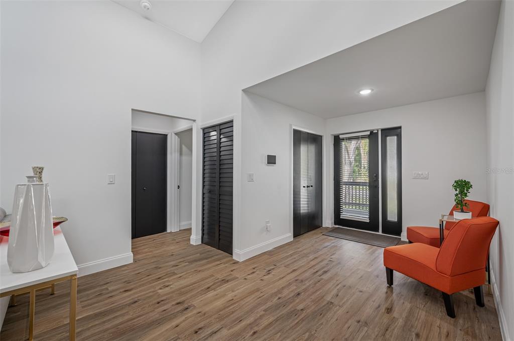 A bright entryway features wood-look flooring, white walls, black doors, and two orange accent chairs — 3717 E CLIFTON STREET, TAMPA, FL