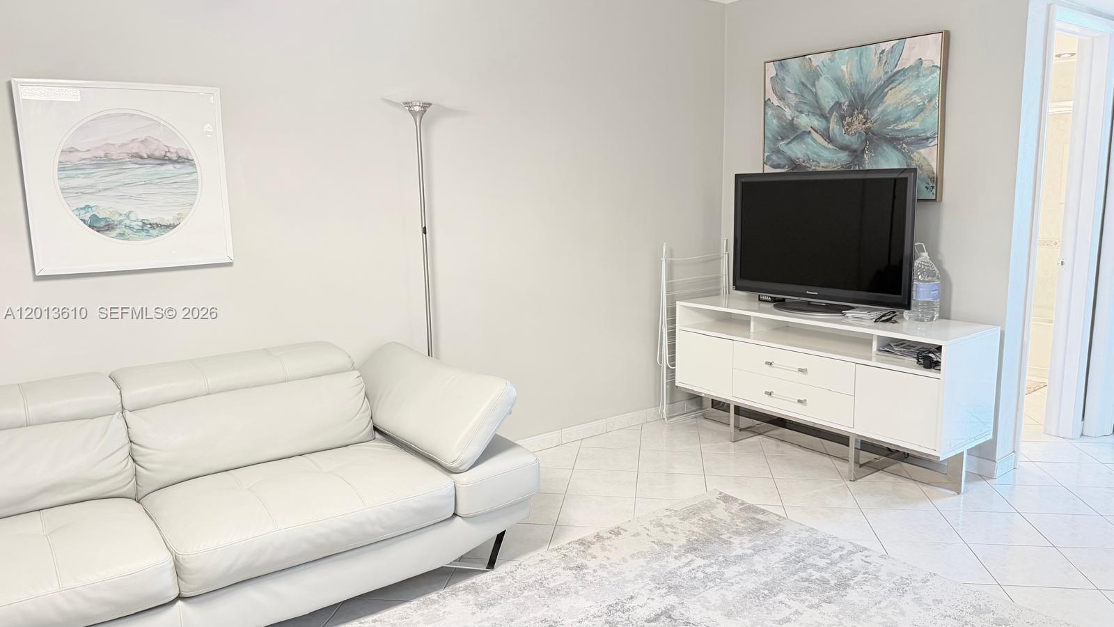 A living room features a white leather sofa, a television console, and wall art — 580 Egret Dr # 211, Hallandale Beach FL 33009, HALLANDALE BEACH, FL