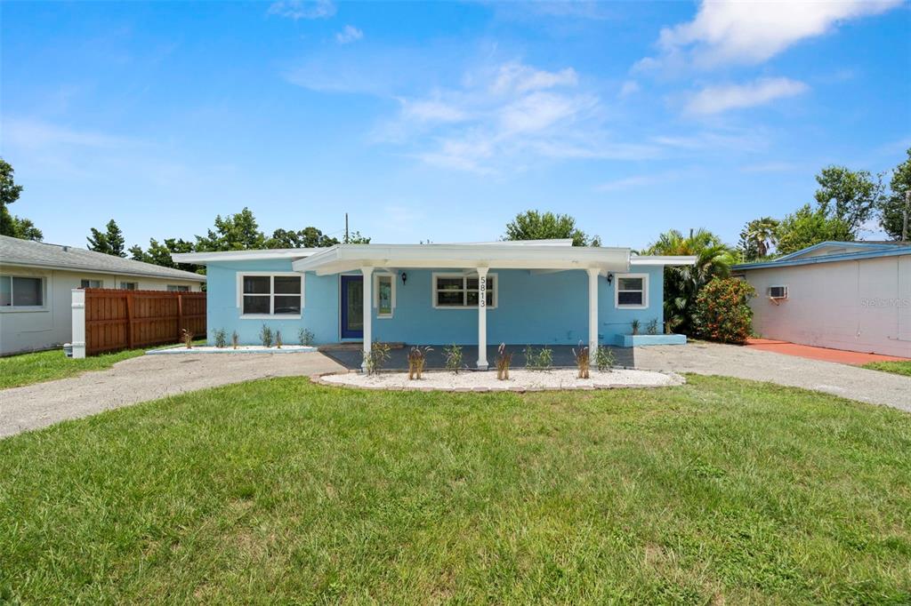 A light blue single-story house features a front carport, white trim, and a gravel driveway — 5813 18TH AVENUE S, GULFPORT, FL
