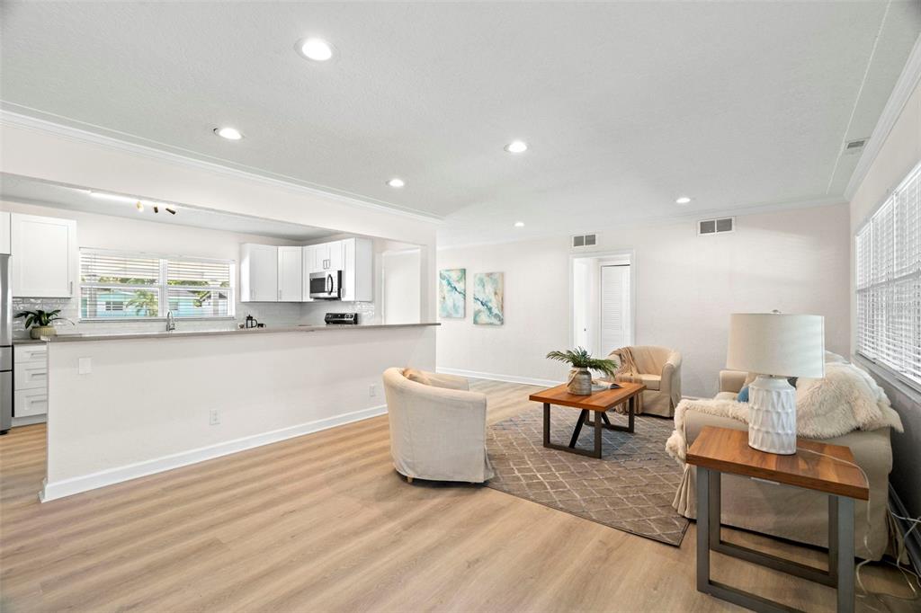 A bright living room with light wood flooring opens to a white kitchen — 5813 18TH AVENUE S, GULFPORT, FL