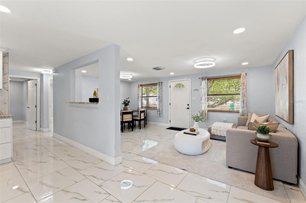 An open-concept living and dining area features white marble-look tile flooring and light blue walls — 1415 BRIXTON LANE, HOLIDAY, FL