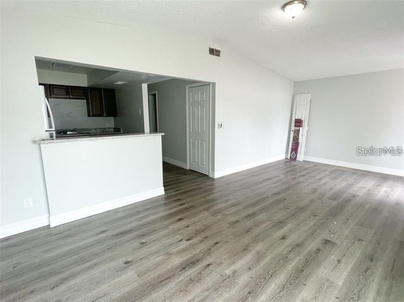 A living room with light gray walls and wood-look flooring features a kitchen pass-through window — 3008 SAINT PAUL DRIVE UNIT 3012, WINTER HAVEN, FL
