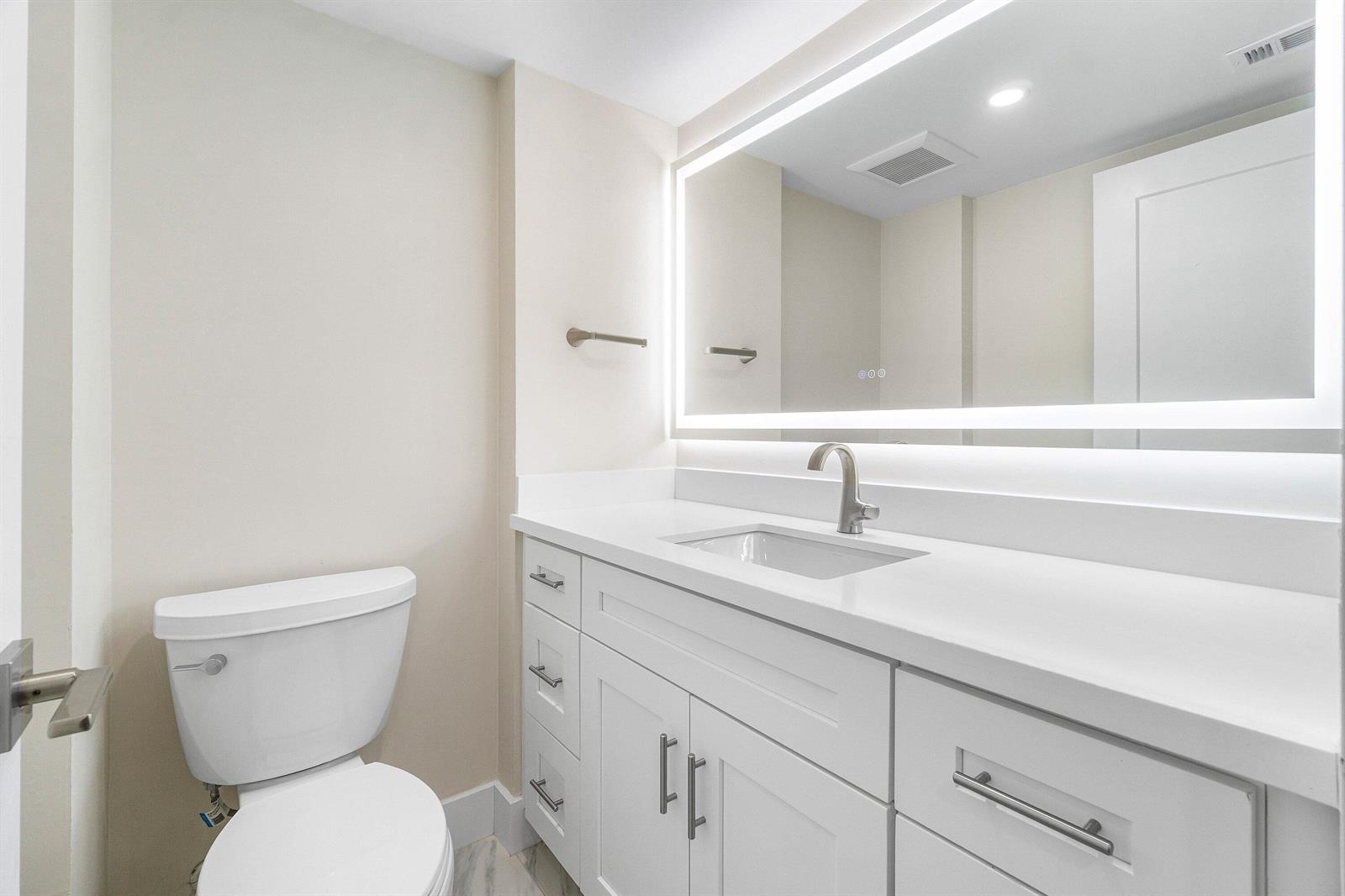 A hallway with light wood flooring, a black metal railing, and a doorway to a bedroom — 16 Stratford Drive E # C, Boynton Beach FL 33436, BOYNTON BEACH, FL