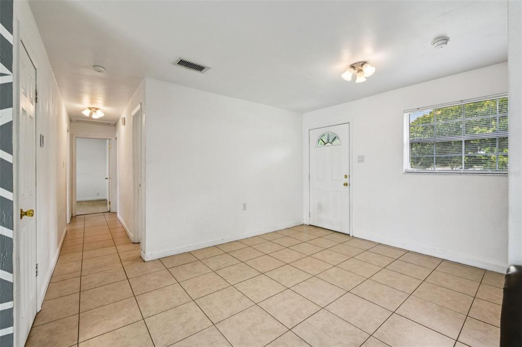 An empty room with beige tile flooring, white walls, a front door, and a window — 911 SHADY PARK TERRACE, DAYTONA BEACH, FL