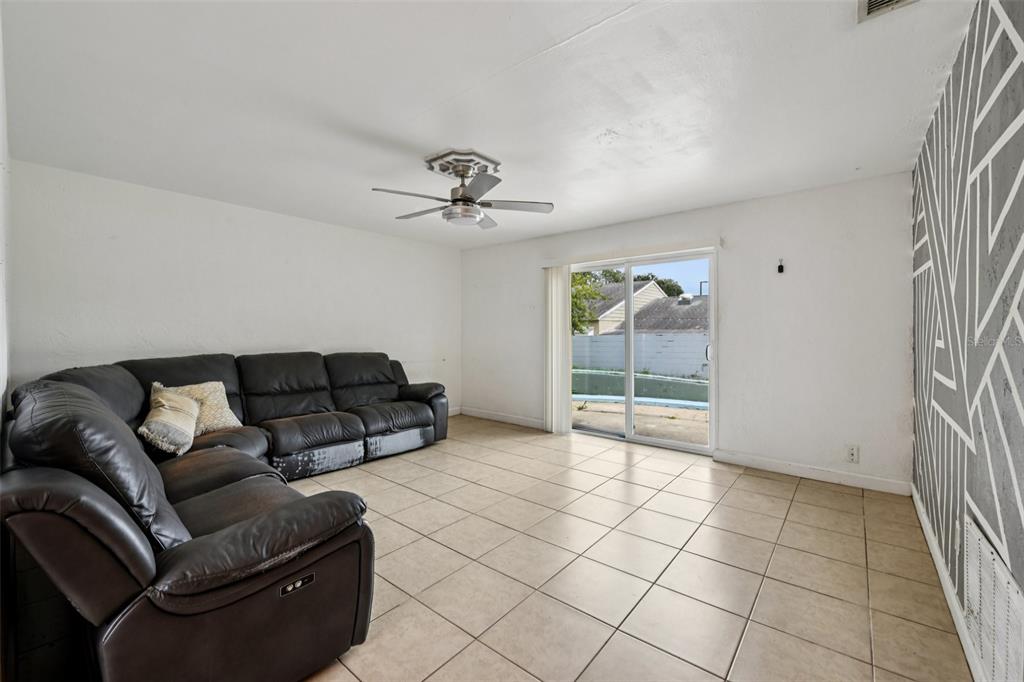 A living room features a dark leather sectional, tile flooring, a ceiling fan, and sliding doors — 911 SHADY PARK TERRACE, DAYTONA BEACH, FL