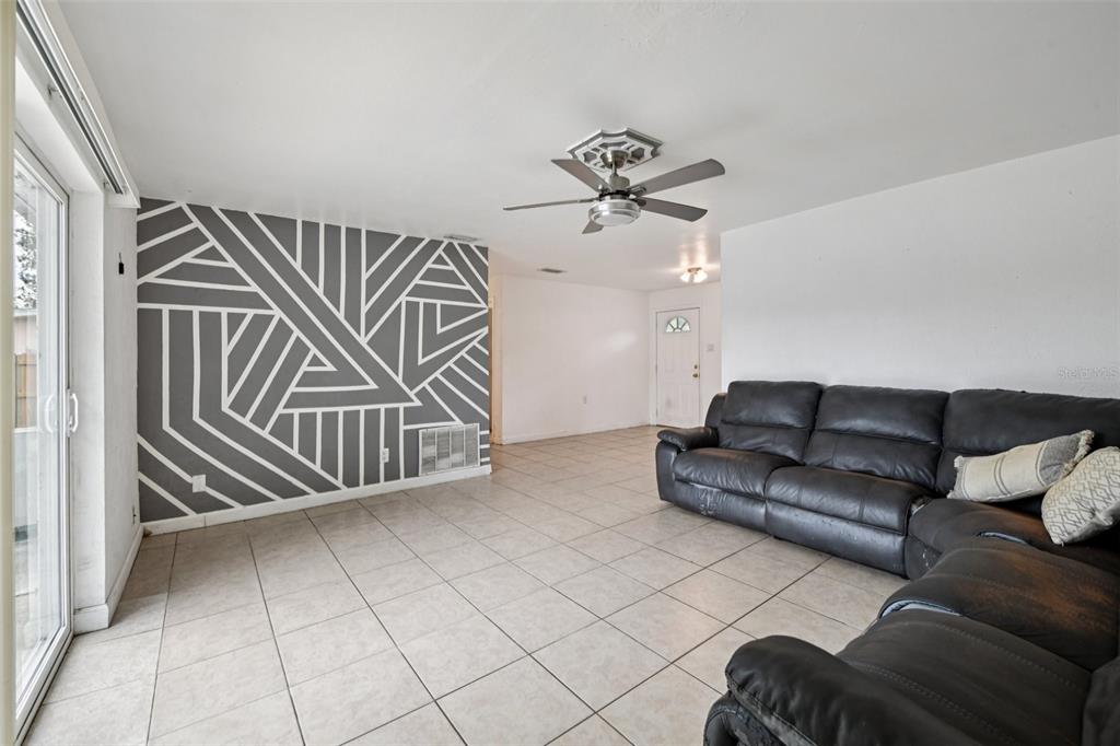 A living room features tile flooring, a geometric accent wall, and a dark leather sectional sofa — 911 SHADY PARK TERRACE, DAYTONA BEACH, FL