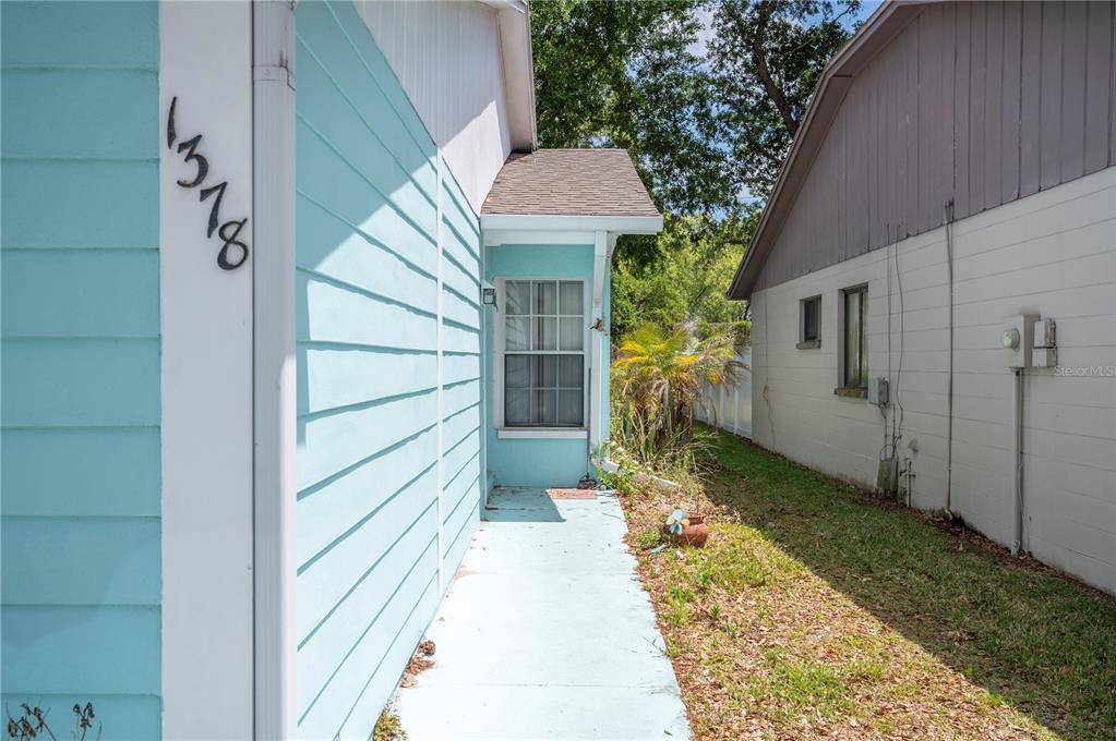 A light blue house exterior features a walkway leading to a window and a side yard — 1378 BRAMBLEWOOD DRIVE, LAKELAND, FL