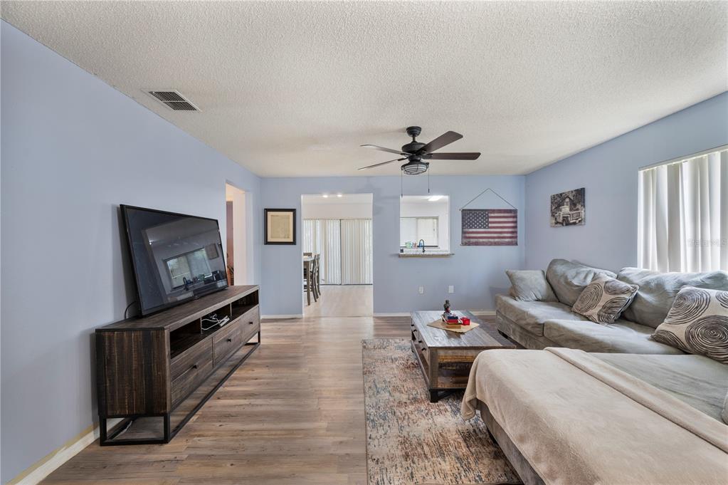 A living room with light blue walls, wood-look flooring, a sectional sofa, and a television — 1378 BRAMBLEWOOD DRIVE, LAKELAND, FL