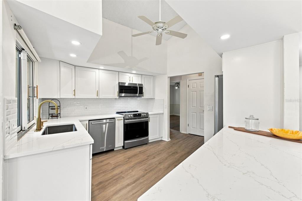 A modern kitchen features white cabinets, stainless steel appliances, and a white quartz island — 13513 WOODSIDE DRIVE, HUDSON, FL