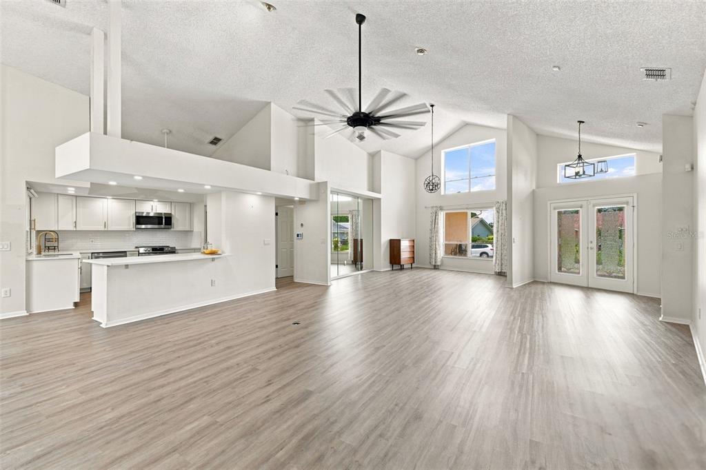 A spacious, open-concept living area with vaulted ceilings, light wood-look flooring, and an attached kitchen — 13513 WOODSIDE DRIVE, HUDSON, FL