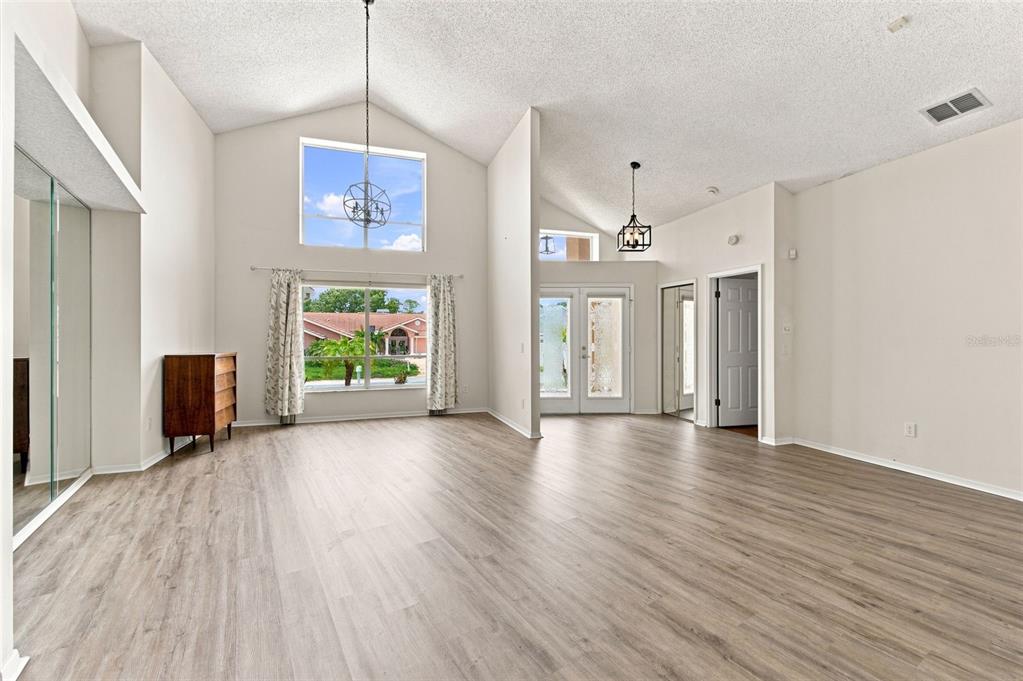 A spacious living room features vaulted ceilings, light wood-look flooring, and a large window — 13513 WOODSIDE DRIVE, HUDSON, FL