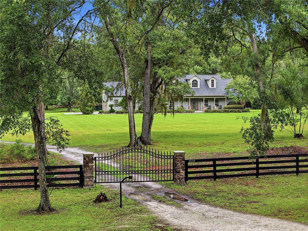A two-story house sits behind a black metal gate and a long, grassy lawn — 21158 NW COUNTY ROAD 2054, ALACHUA, FL