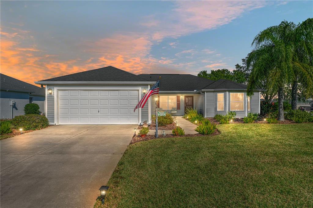 A single-story house with gray siding, a two-car garage, and a front lawn at sunset — 3073 RIVERDALE ROAD, THE VILLAGES, FL