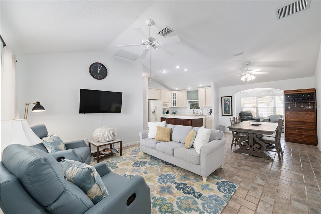 An open-concept living and dining area features tile floors, a vaulted ceiling, and neutral furniture — 3073 RIVERDALE ROAD, THE VILLAGES, FL