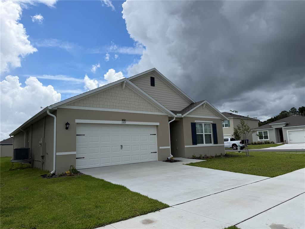 A single-story suburban house with a two-car garage, beige stucco siding, and a concrete driveway — 3307 WYNWOOD FOREST DRIVE, OCOEE, FL