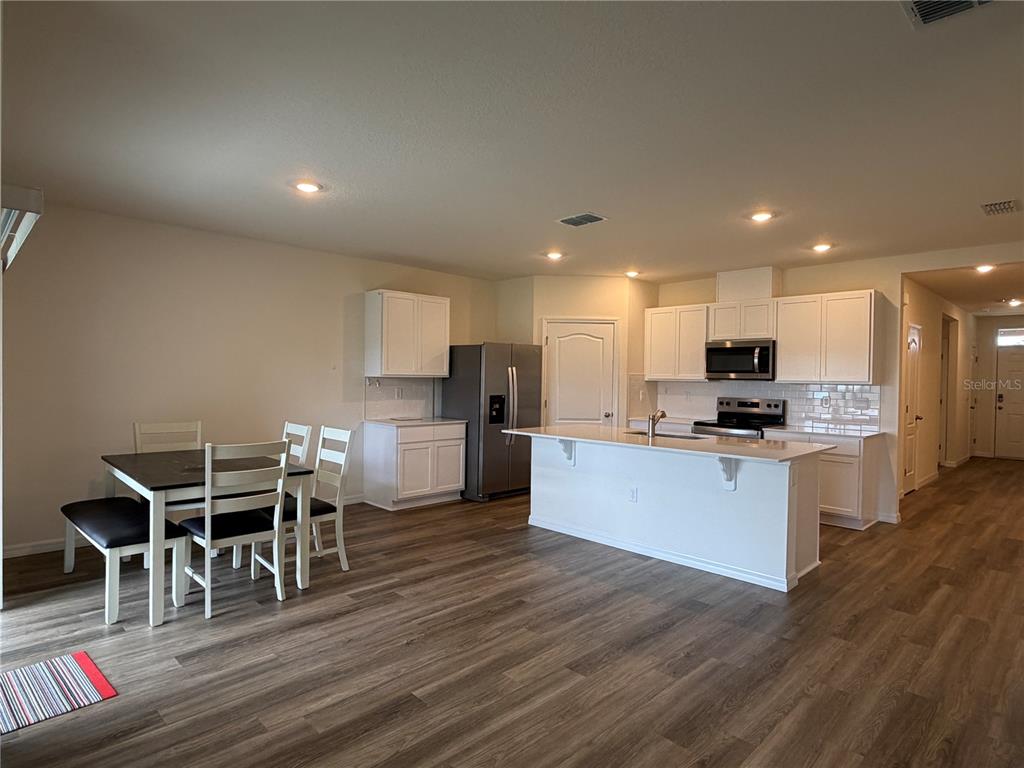 An open-concept kitchen and dining area features white cabinets, a center island, and wood-look flooring — 3307 WYNWOOD FOREST DRIVE, OCOEE, FL