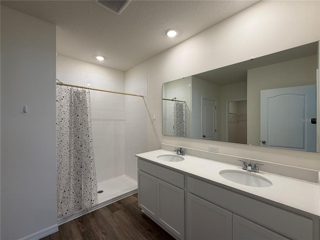 A bathroom features a double vanity, a walk-in shower with a curtain, and wood-look flooring — 3307 WYNWOOD FOREST DRIVE, OCOEE, FL