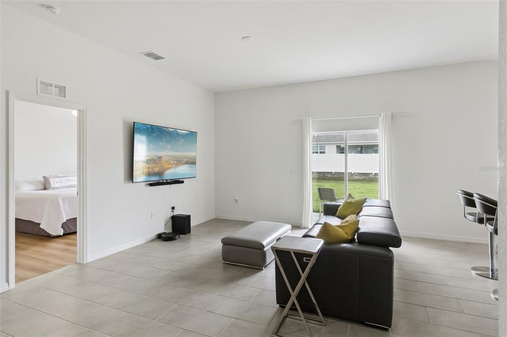 A living room with tile flooring, a wall-mounted television, a sofa, and a sliding glass door — 1225 PINTAIL PLACE, LAKELAND, FL