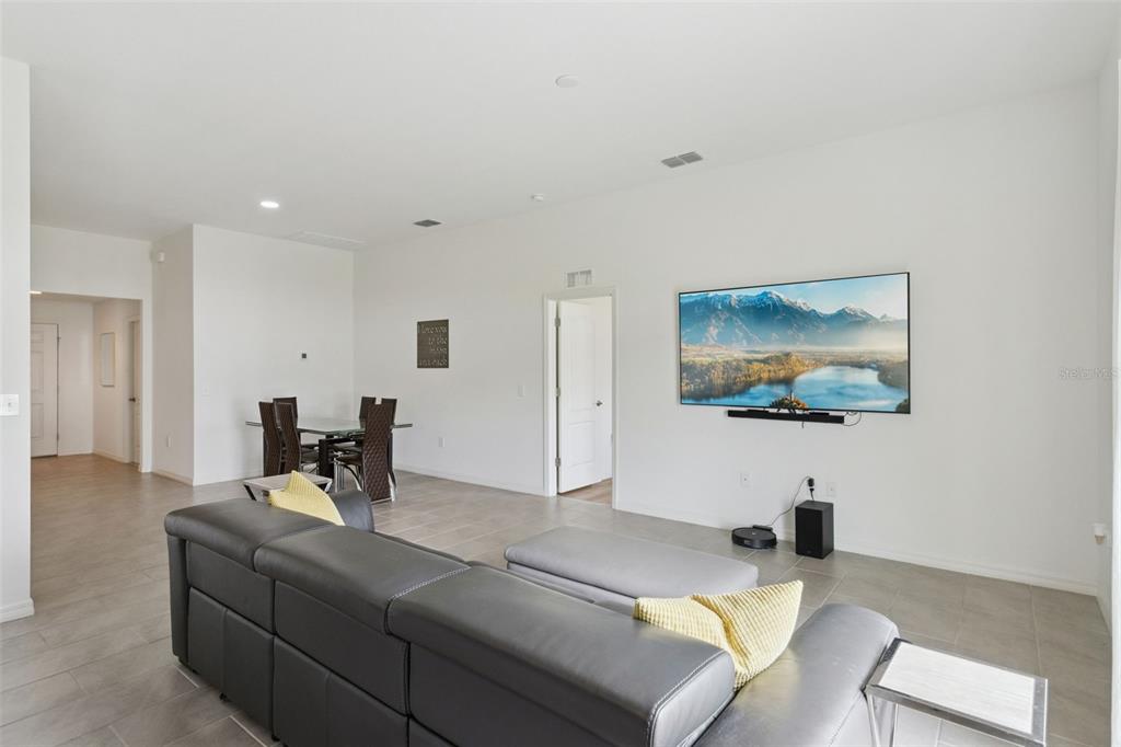A living room with gray tile flooring, a large sectional sofa, and a wall-mounted television — 1225 PINTAIL PLACE, LAKELAND, FL