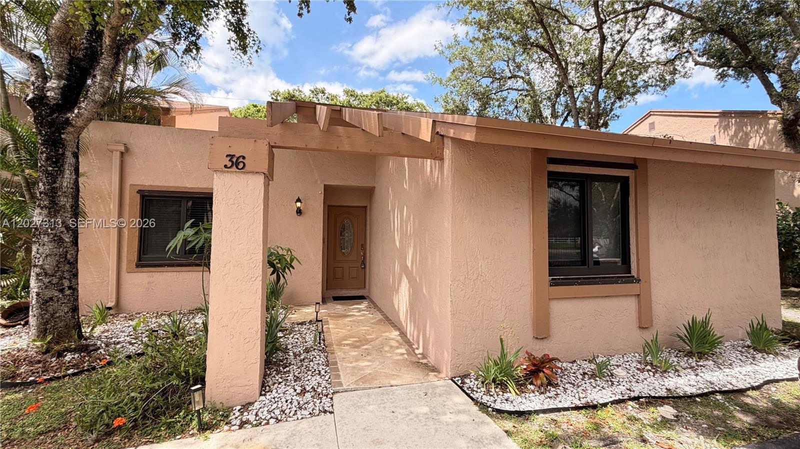 The exterior of a single-story tan stucco home features a wooden pergola and walkway — 36 Chestnut Cir, # 36, Cooper City FL 33026, COOPER CITY, FL