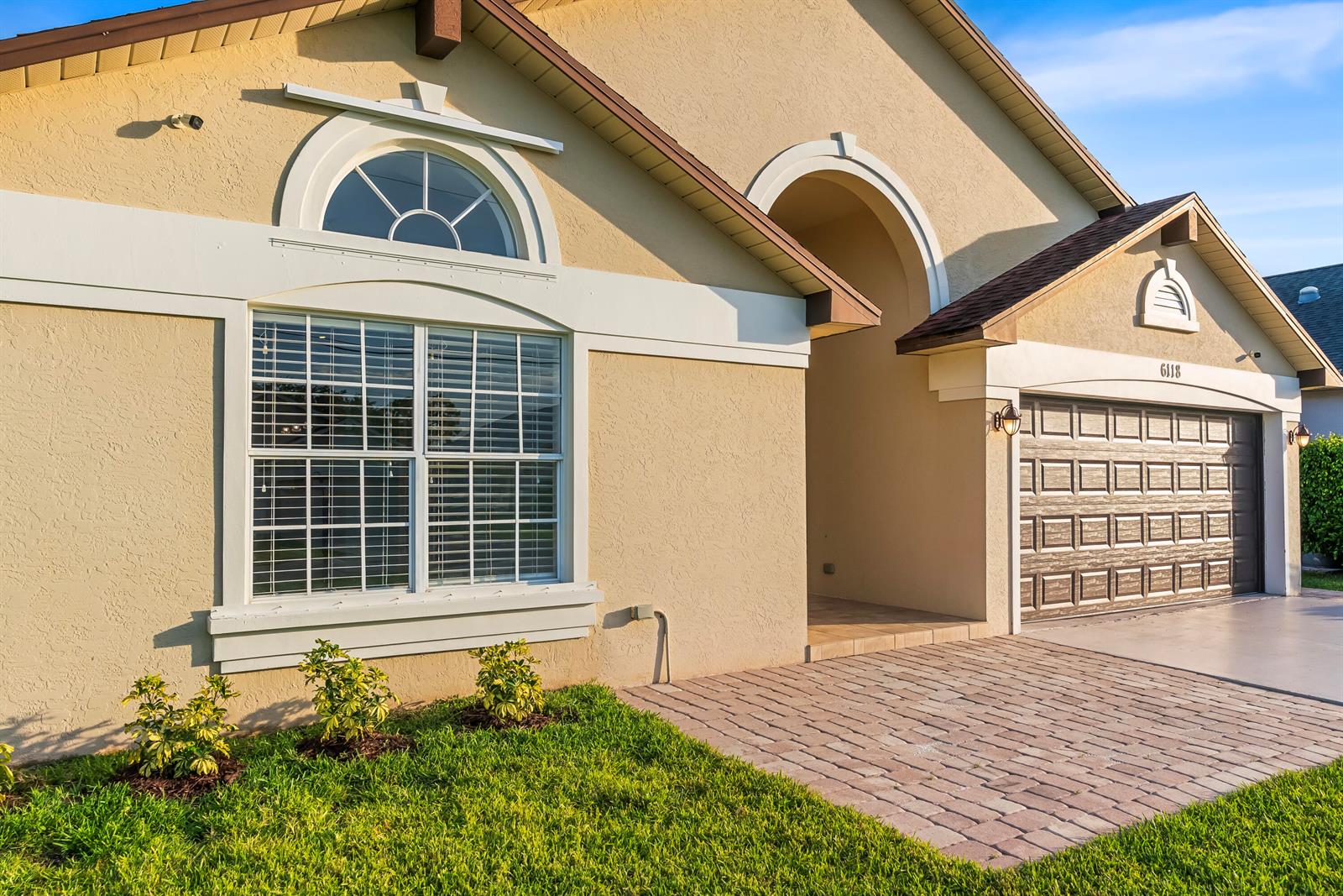 A tan stucco house features a arched window, a covered entryway, and a two-car garage — 6118 Pompano Street, Jupiter FL 33458, JUPITER, FL