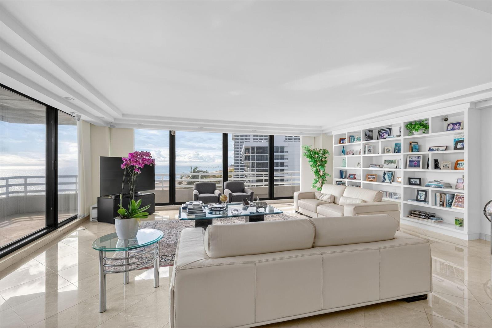A bright living room features white leather sofas, a glass coffee table, and built-in shelving — 1500 S Ocean Boulevard # 606, Boca Raton FL 33432, BOCA RATON, FL