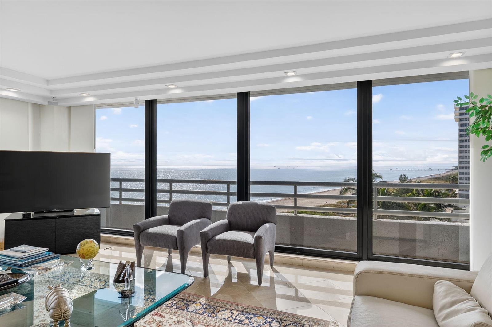 A living room with a glass coffee table and two chairs facing a beach view — 1500 S Ocean Boulevard # 606, Boca Raton FL 33432, BOCA RATON, FL