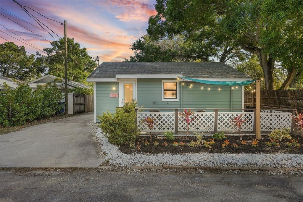 A light green cottage with a white lattice deck, string lights, and a paved driveway — 3027 BURLINGTON AVENUE N, ST PETERSBURG, FL