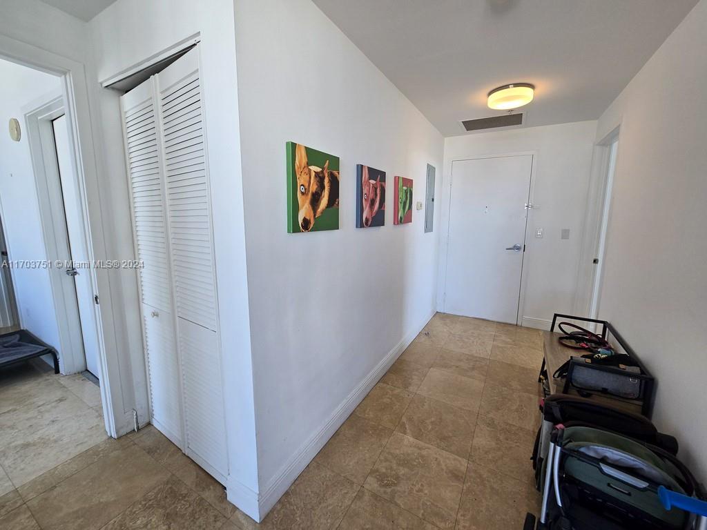 A hallway with tiled floors, white walls, three pet portraits, and a white entry door — 3470 E Coast Ave # H1404, Miami FL 33137, MIAMI, FL