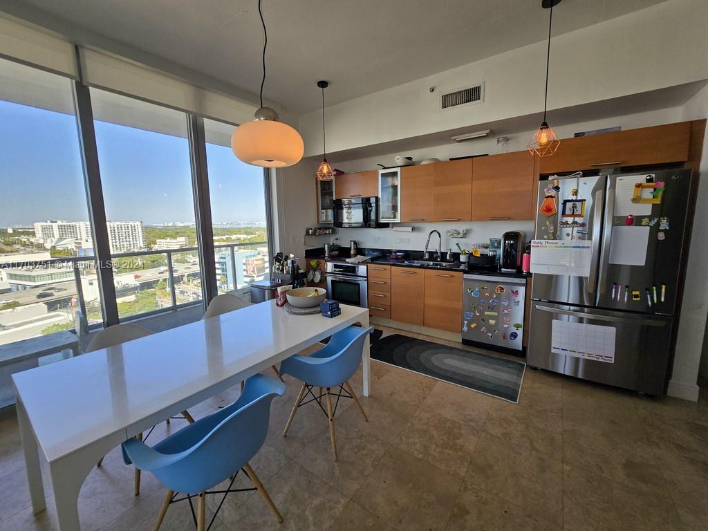 A kitchen and dining area features light wood cabinetry, stainless steel appliances, and floor-to-ceiling windows — 3470 E Coast Ave # H1404, Miami FL 33137, MIAMI, FL