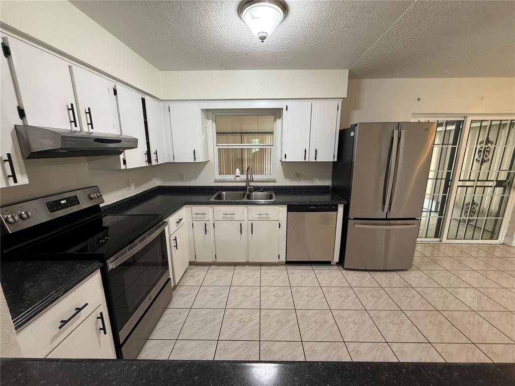 A kitchen features white cabinets, stainless steel appliances, dark countertops, and light-colored tiled flooring — 202 YALE DRIVE, SANFORD, FL