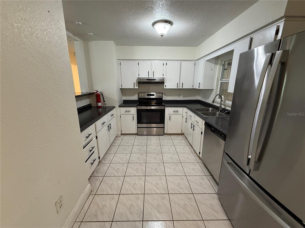 A kitchen features white cabinets, stainless steel appliances, dark countertops, and light-colored tile flooring — 202 YALE DRIVE, SANFORD, FL