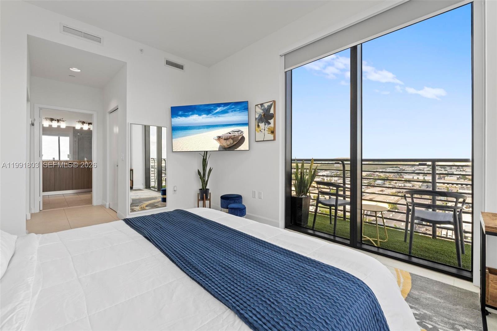 A bedroom features a bed, wall-mounted television, and a balcony with outdoor seating and views — 5350 NW 84th Ave # 2013, Doral FL 33166, DORAL, FL