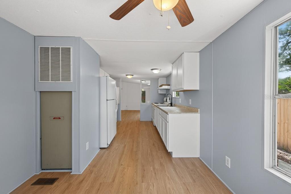 A galley-style kitchen features white cabinets, light wood-look flooring, and light blue walls — 11711 TUCKER ROAD, RIVERVIEW, FL