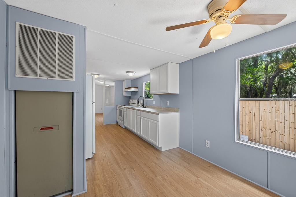 A kitchen with white cabinets, light wood-look flooring, and a ceiling fan in the foreground — 11711 TUCKER ROAD, RIVERVIEW, FL