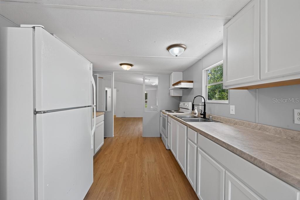 A kitchen with white cabinets, light countertops, wood-look flooring, and a white refrigerator — 11711 TUCKER ROAD, RIVERVIEW, FL