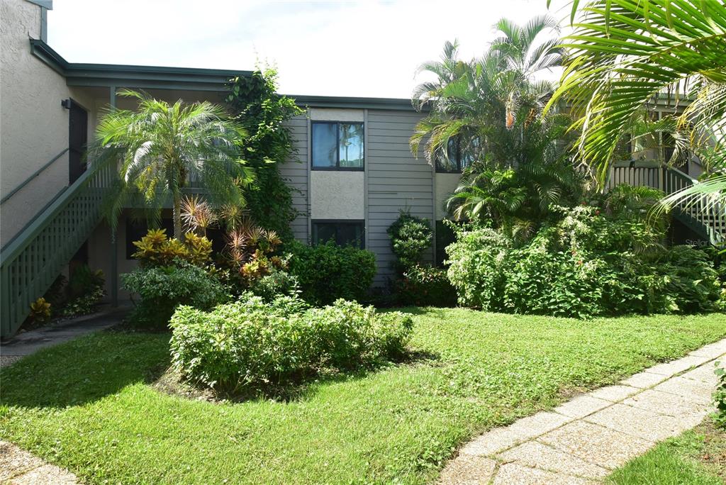 A two-story apartment building exterior with a green staircase, landscaping, and a stone walkway — 1520 PELICAN POINT DRIVE UNIT BA153, SARASOTA, FL