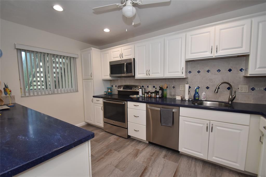 A kitchen features white cabinets, blue countertops, stainless steel appliances, and wood-look tile flooring — 1520 PELICAN POINT DRIVE UNIT BA153, SARASOTA, FL
