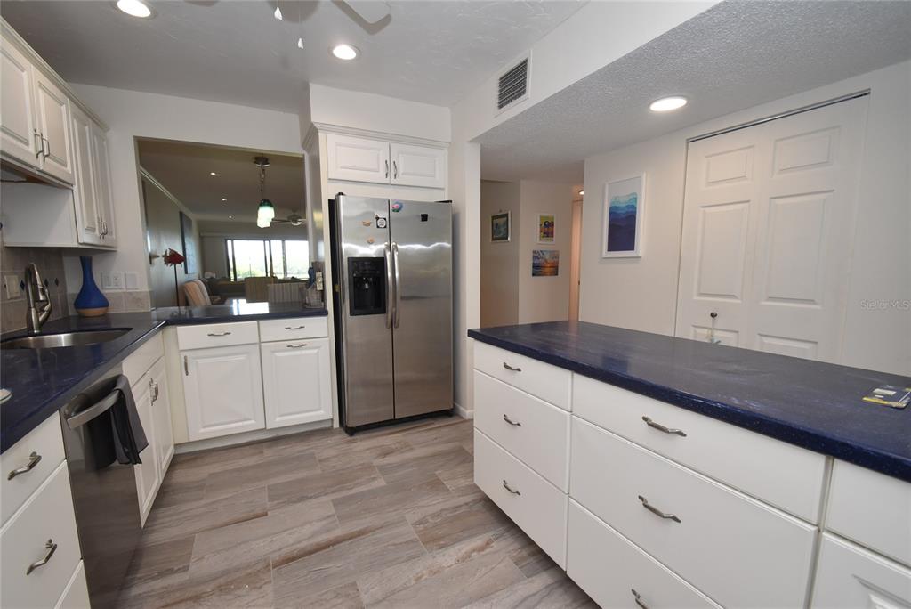 A kitchen features white cabinets, blue countertops, stainless steel appliances, and wood-look tile flooring — 1520 PELICAN POINT DRIVE UNIT BA153, SARASOTA, FL