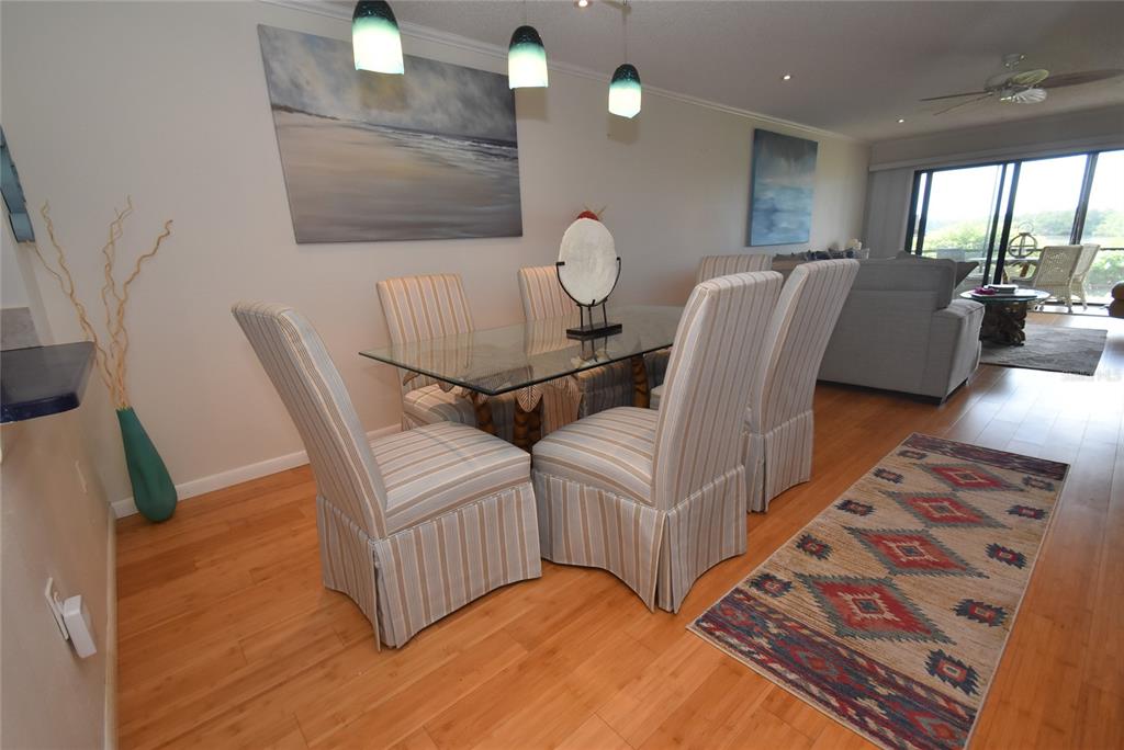 A dining area features a glass-topped table, striped chairs, pendant lights, and hardwood flooring — 1520 PELICAN POINT DRIVE UNIT BA153, SARASOTA, FL