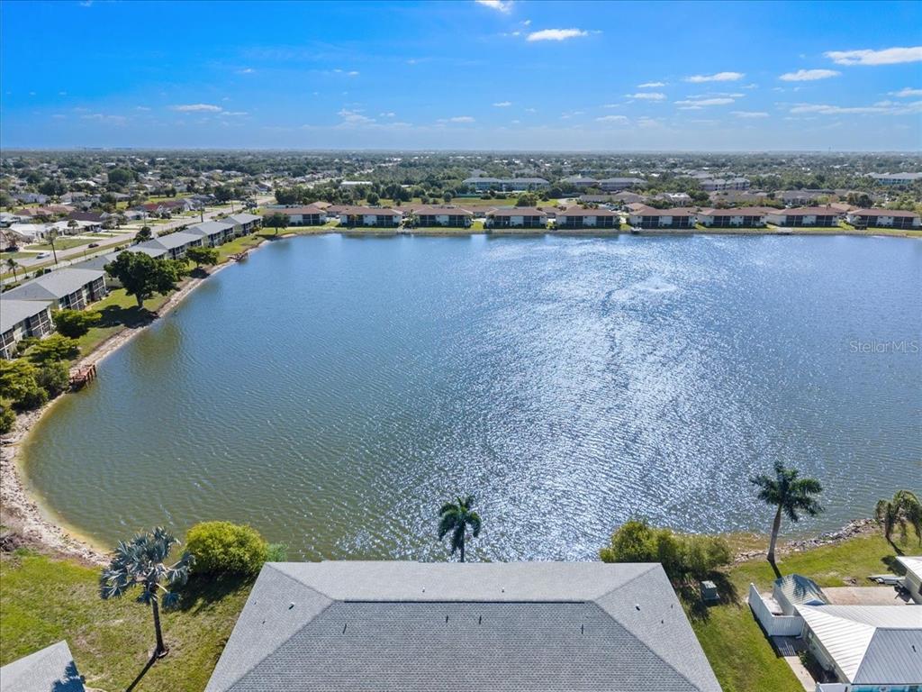 An aerial view shows a residential building overlooking a large lake with distant housing — 25225 RAMPART BOULEVARD UNIT 1207, PUNTA GORDA, FL