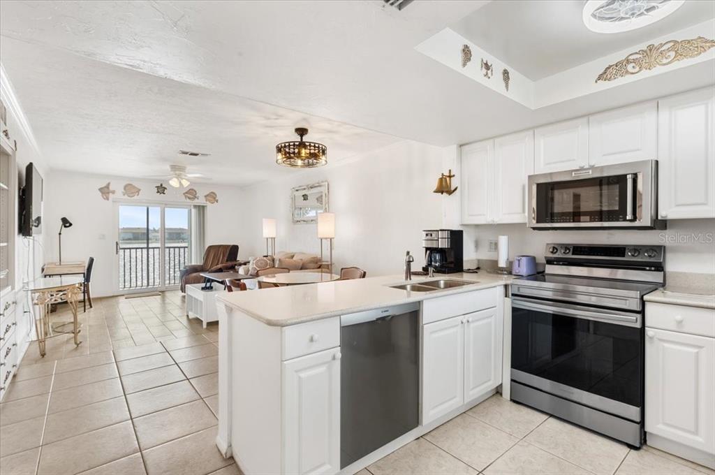 A kitchen with white cabinets and stainless steel appliances opens into a living area — 25225 RAMPART BOULEVARD UNIT 1207, PUNTA GORDA, FL
