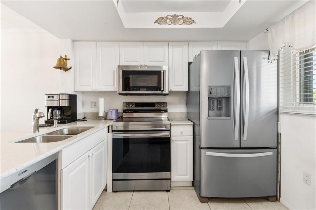 A kitchen features white cabinets, stainless steel appliances, and light-colored countertops — 25225 RAMPART BOULEVARD UNIT 1207, PUNTA GORDA, FL