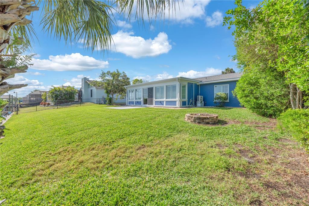 A blue house with a sunroom and a stone fire pit in the backyard — 911 SILVER PALM WAY, APOLLO BEACH, FL