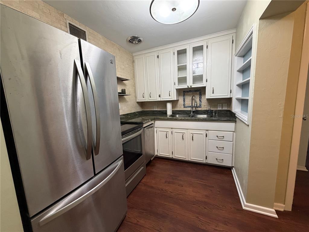 A kitchen features white cabinets, stainless steel appliances, dark countertops, and wood-look flooring — 701 SW 28TH STREET, GAINESVILLE, FL