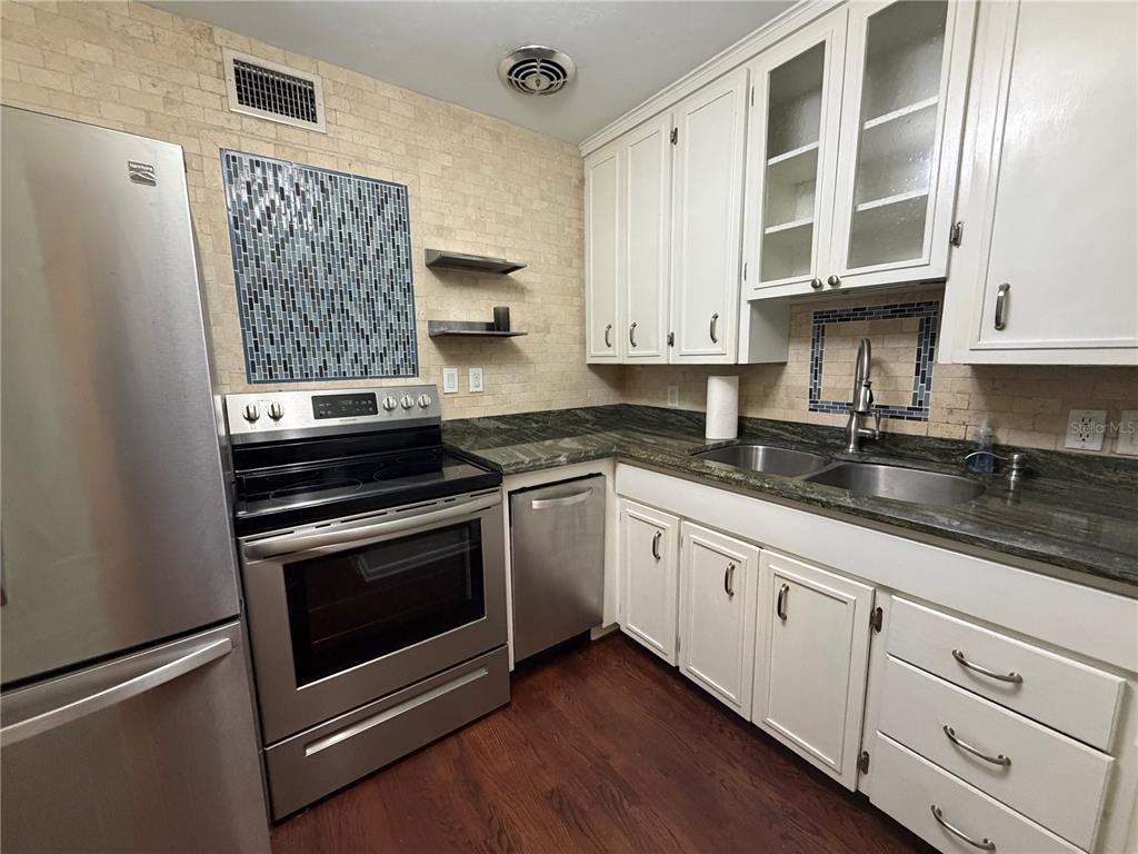 A kitchen with white cabinets, stainless steel appliances, dark countertops, and a blue tile backsplash — 701 SW 28TH STREET, GAINESVILLE, FL